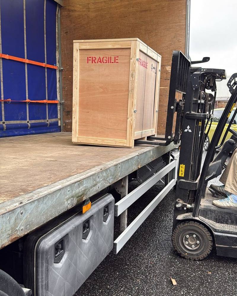 Forklift loading a wooden crate marked fragile onto an 18-tonne curtainsider