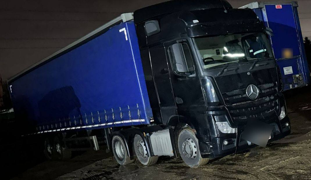 Black Mercedes Actros coupled to a blue curtainside trailer in a yard at night