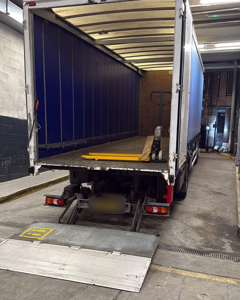 18-tonne curtainsider backed into a loading bay with the tail lift lowered and a pallet truck on board